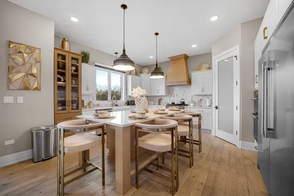 a kitchen with stainless steel appliances kitchen island granite countertop a refrigerator a stove a sink a dining table and chairs with wooden floor