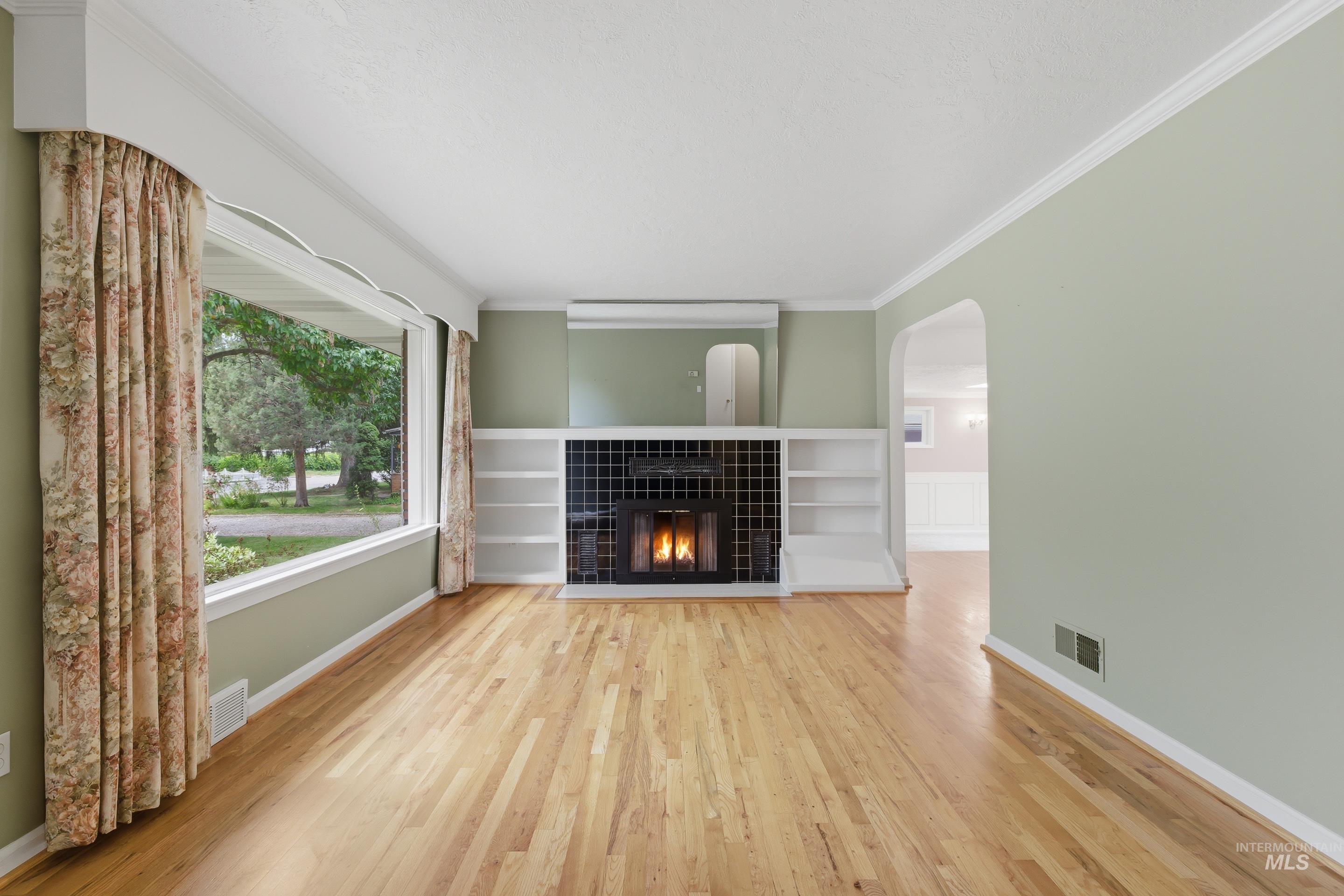 504 West Howe Street Boise, ID 83706 - Photo 5 of 47 Living area featuring wood-finish flooring, a tiled fireplace with mantel, built-in shelving, and a large picture window