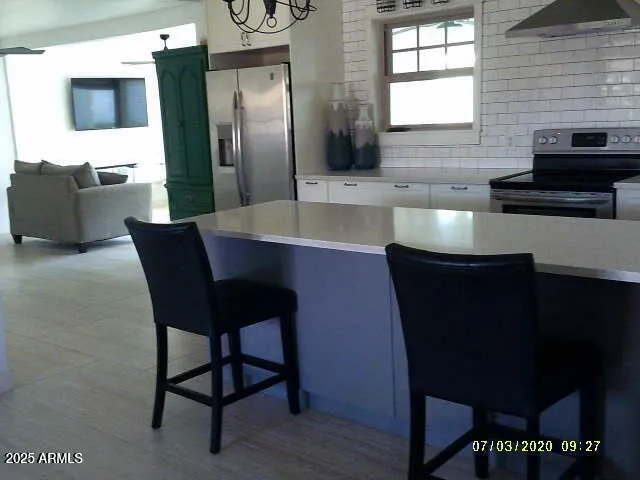 a kitchen with stainless steel appliances granite countertop a dining table chairs cabinets a sink and a window