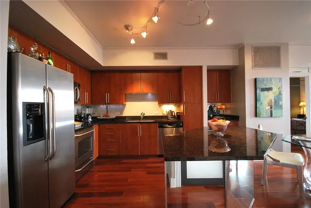 a kitchen with stainless steel appliances kitchen island granite countertop a refrigerator a stove and a sink with wooden floor