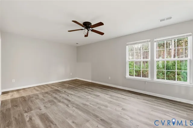 a view of empty room with wooden floor and fan
