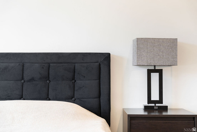 1693 Devils Gdn Lane Washington, UT 84780 - Photo 32 of 64 Tufted headboard with a dark fabric finish, accompanied by a modern bedside lamp with a rectangular shade, set on a dark wood-finish nightstand