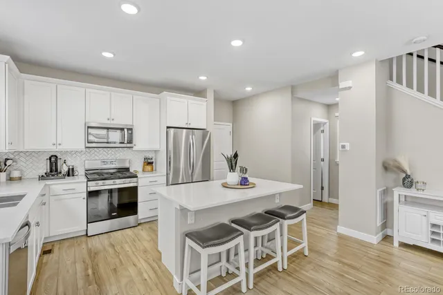 a kitchen with stainless steel appliances a stove a sink a refrigerator white cabinets and wooden floor