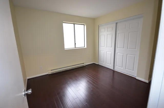 an empty room with wooden floor and windows with curtains