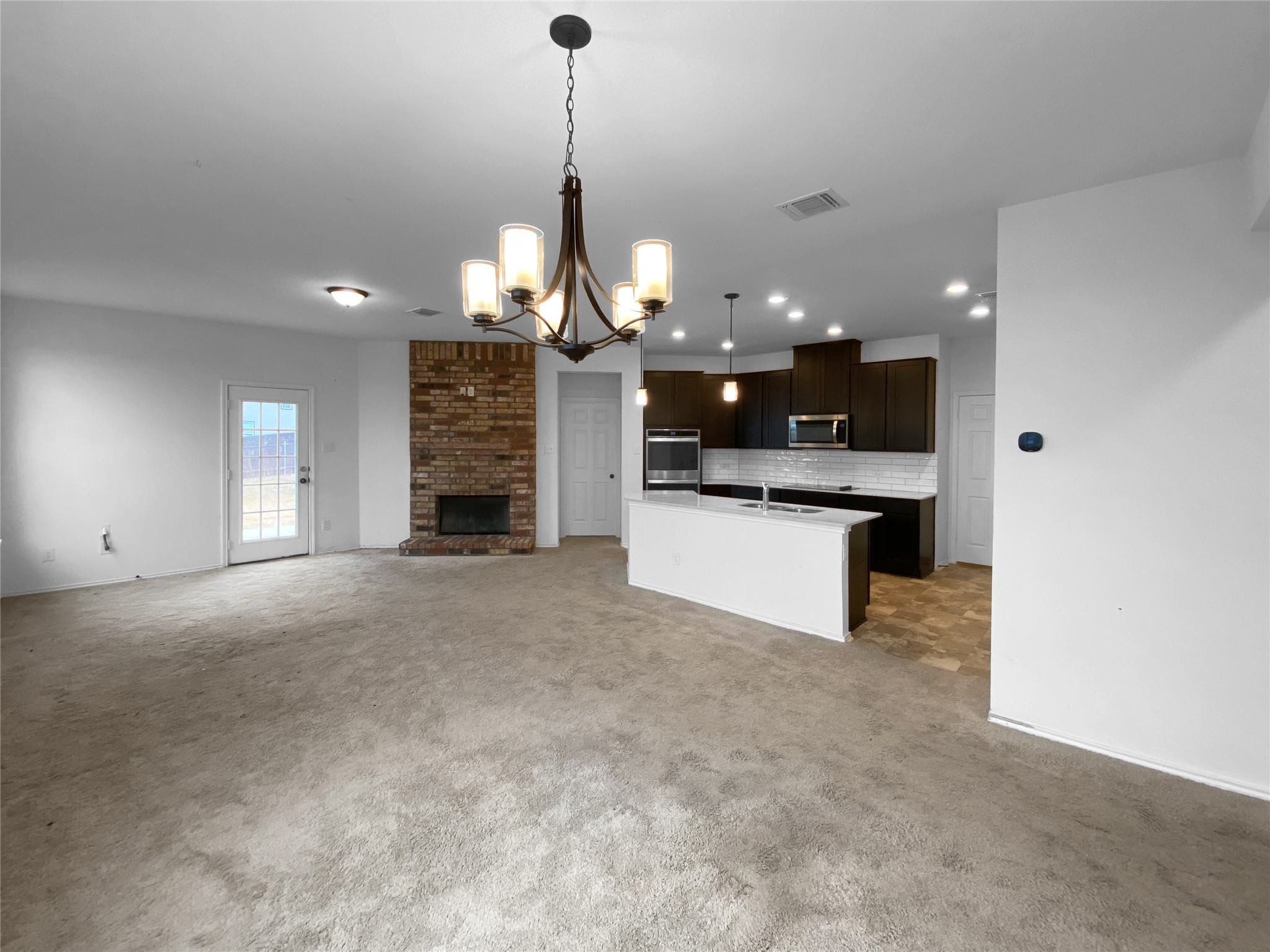 932 Yellow Ribbon Trail Jarrell, TX 76537 - Photo 22 of 26 Kitchen with open floor plan, hanging lights, a center island with sink, dark wood finish cabinets, and tasteful backsplash