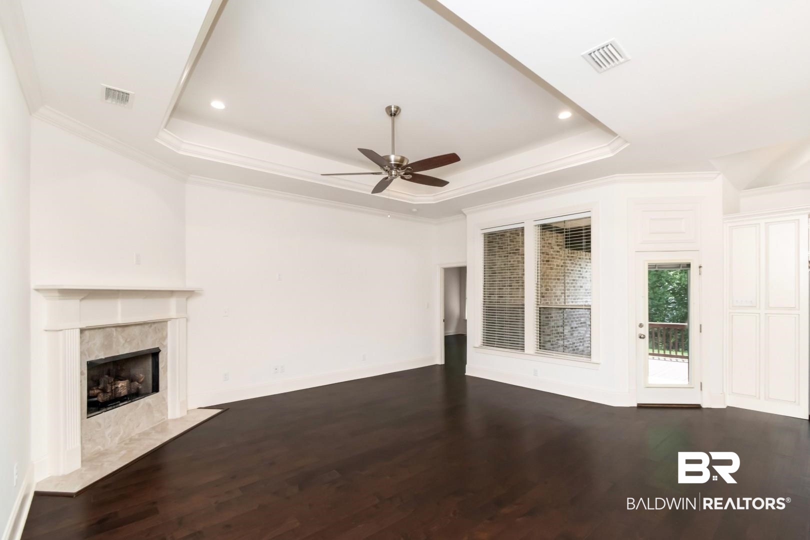 3528 Rue Royal Mobile, AL 36693 - Photo 16 of 53 Expansive living area featuring rich wood-finish flooring, a tray ceiling with recessed lighting and a ceiling fan, a fireplace with a stone surround and mantel, large windows, and built-in cabinetry