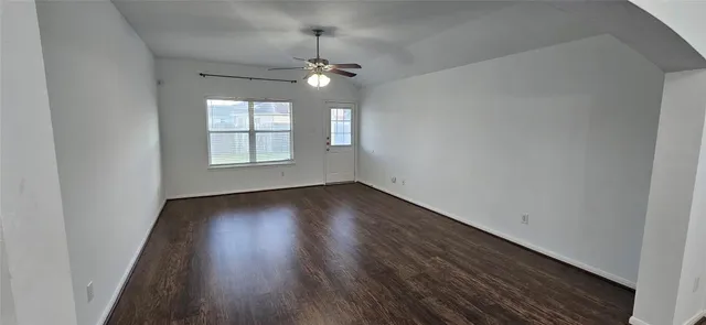 an empty room with wooden floor chandelier fan and windows