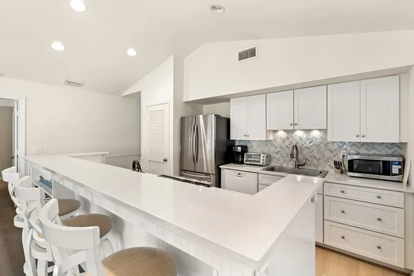 a kitchen with granite countertop a sink a stove a refrigerator and white cabinets with wooden floor