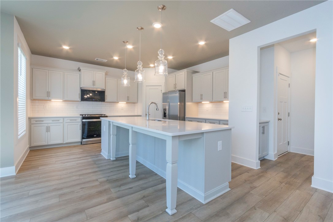 607 WH Kay Lane Anderson, SC 29621 - Photo 6 of 48 A well-lit kitchen boasts an expansive island with a sink and pendant lighting, complementing the plentiful cabinetry and modern appliances.