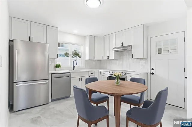 a kitchen with stainless steel appliances granite countertop a dining table chairs refrigerator and sink