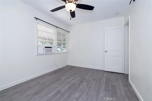 an empty room with wooden floor chandelier fan and windows