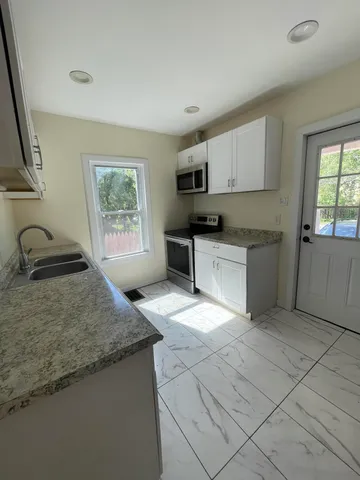 a view of an empty room and kitchen space with a sink