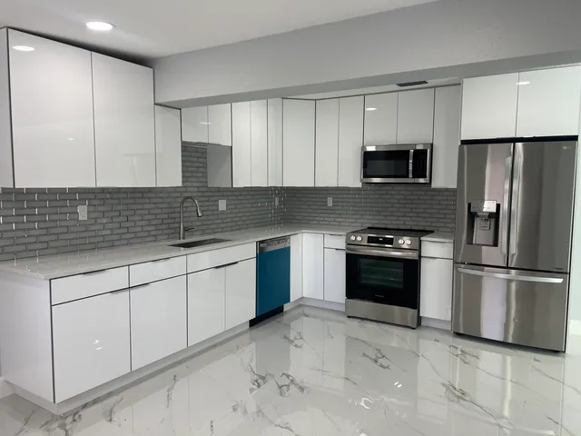 a large white kitchen with stainless steel appliances a sink a stove a microwave and cabinets