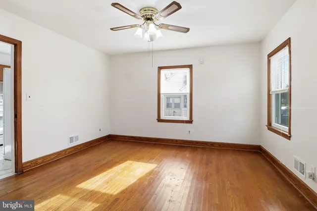 an empty room with wooden floor chandelier fan and windows