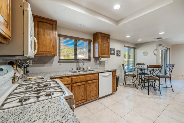 a kitchen with stainless steel appliances granite countertop a stove top oven a sink a dining table and chairs with wooden floor