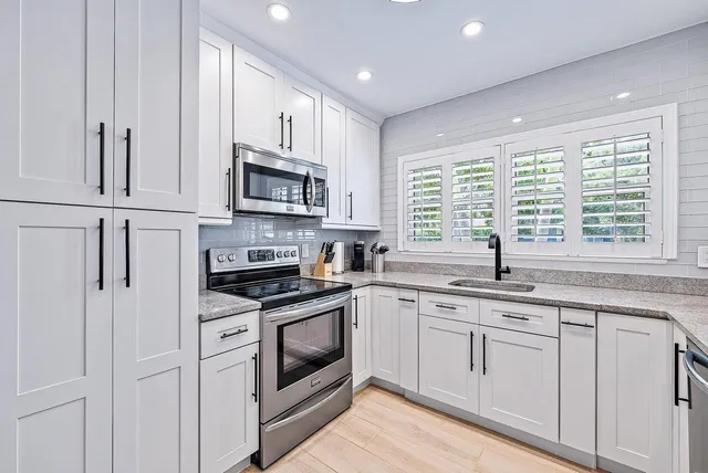 a kitchen with granite countertop white cabinets white stainless steel appliances a sink and a window
