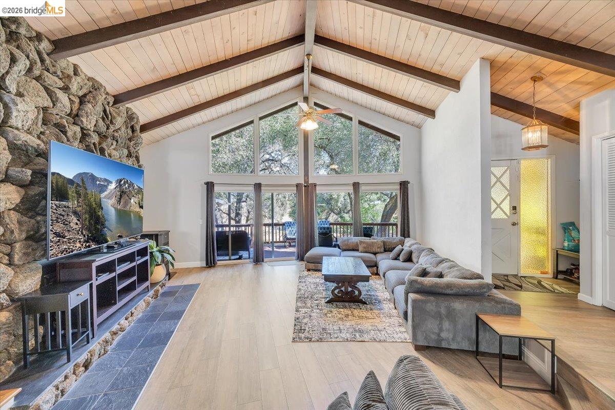 8733 Fraguero Road Sonora, CA 95370 - Photo 21 of 73 Vaulted wood plank ceilings with exposed beams, stone fireplace with slate hearth, floor-to-ceiling windows, wood-finish flooring, and a glass-paneled entry door