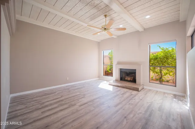 an empty room with windows a fireplace and a ceiling fan