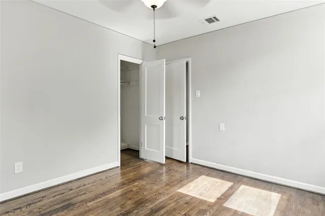 a view of an empty room with wooden floor and a ceiling fan