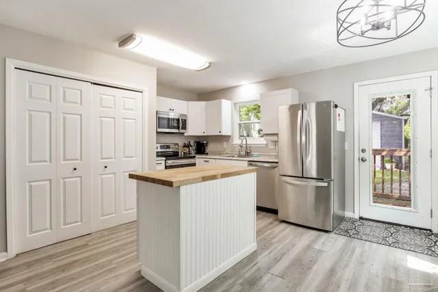 a kitchen with stainless steel appliances a stove a sink dishwasher a refrigerator white cabinets and wooden floor