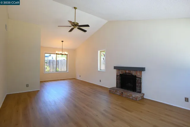 an empty room with wooden floor a ceiling fan and windows