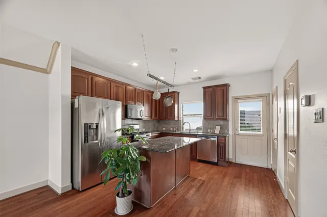 a kitchen with stainless steel appliances granite countertop a refrigerator a sink a stove and wooden floors