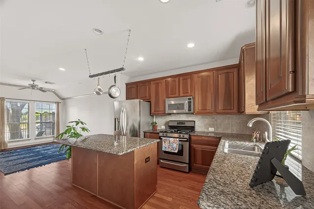 a kitchen with stainless steel appliances granite countertop a stove top oven a sink dishwasher a dining table and chairs with wooden floor