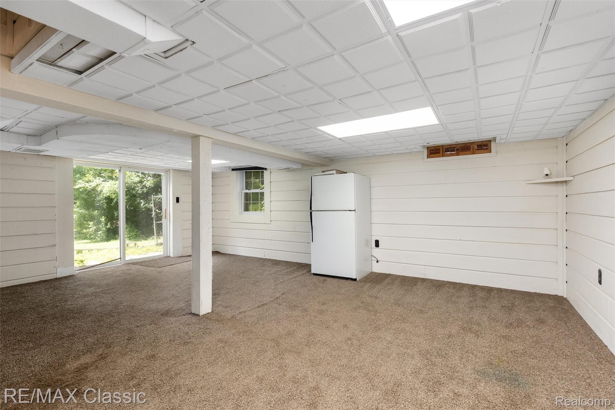 4268 Covered Bridge Road Bloomfield Hills, MI 48302 - Photo 23 of 35 Carpeted interior space featuring a drop ceiling with integrated lighting, shiplap-style wall paneling, and a full-light sliding glass door