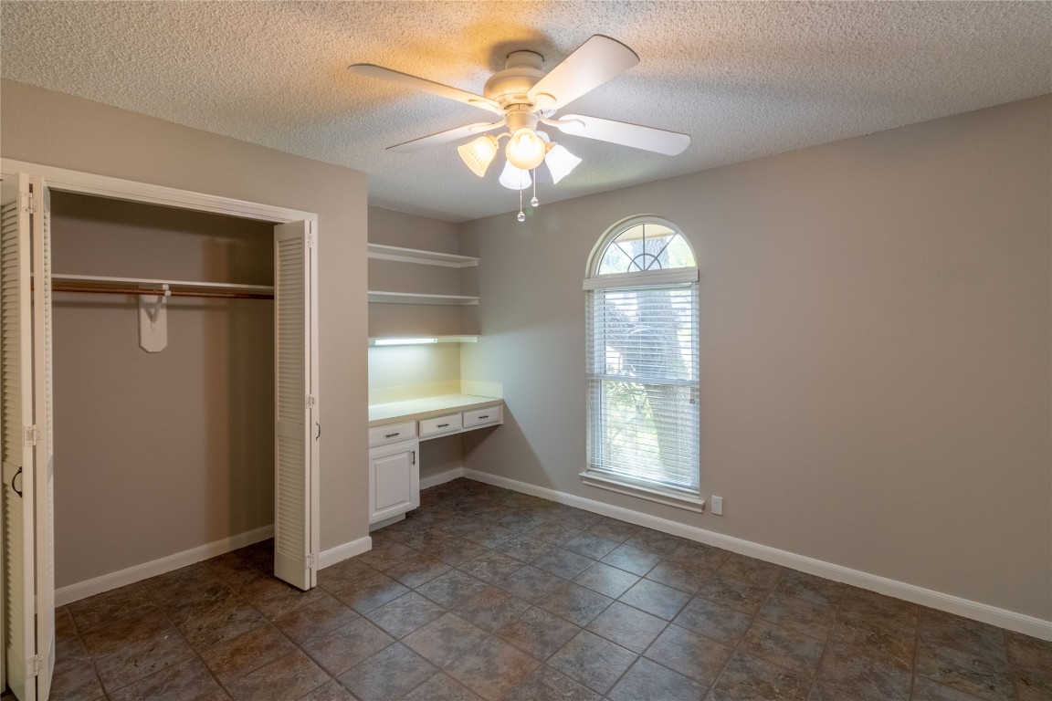 5839 Secrest Drive Austin, TX 78759 - Photo 12 of 34 Unfurnished bedroom featuring built in desk, a textured ceiling, a closet, and ceiling fan