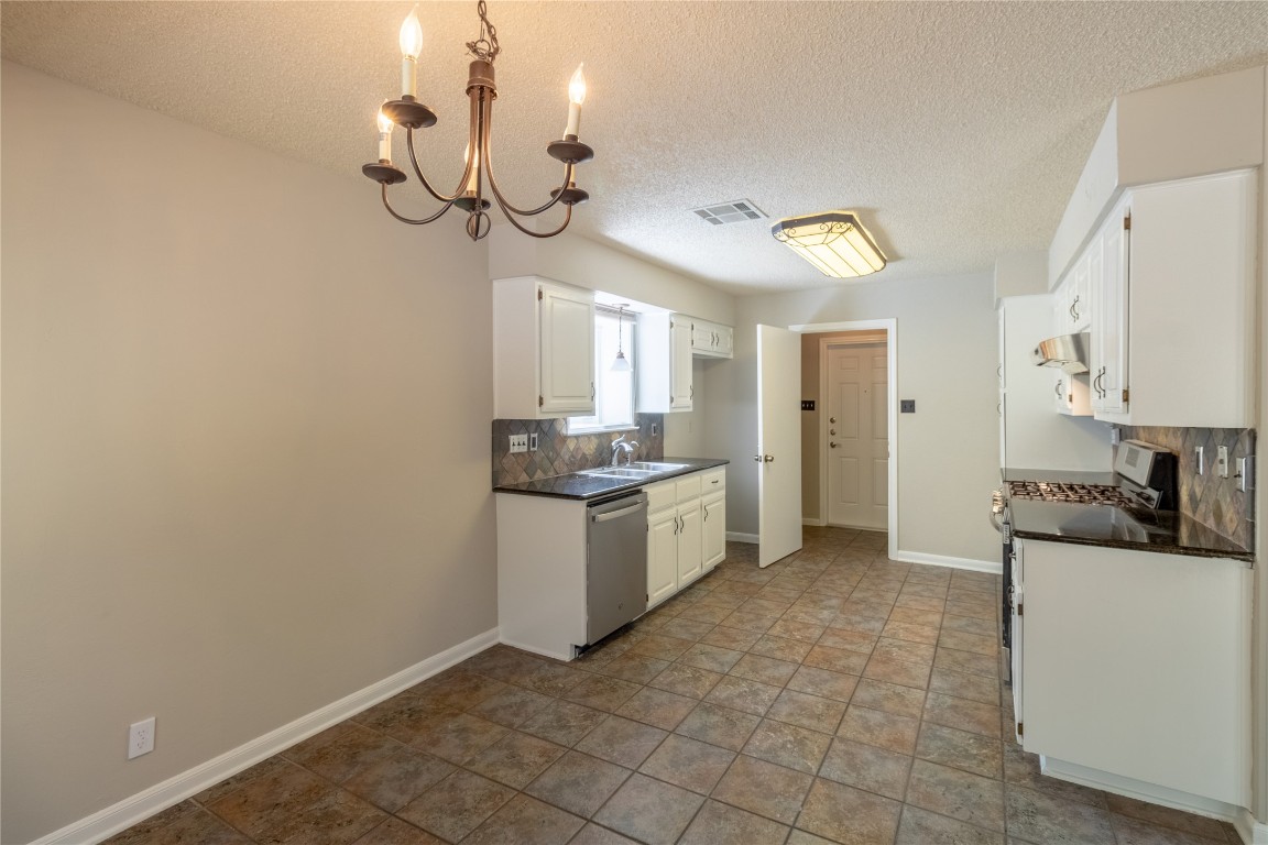5839 Secrest Drive Austin, TX 78759 - Photo 21 of 34 Kitchen featuring stainless steel appliances, decorative backsplash, dark countertops, under cabinet range hood, and a chandelier