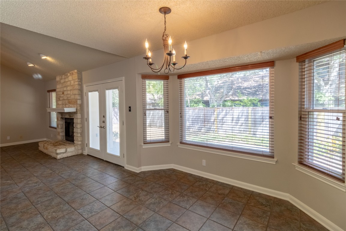5839 Secrest Drive Austin, TX 78759 - Photo 22 of 34 Unfurnished dining area featuring a stone fireplace, a chandelier, a textured ceiling, and lofted ceiling