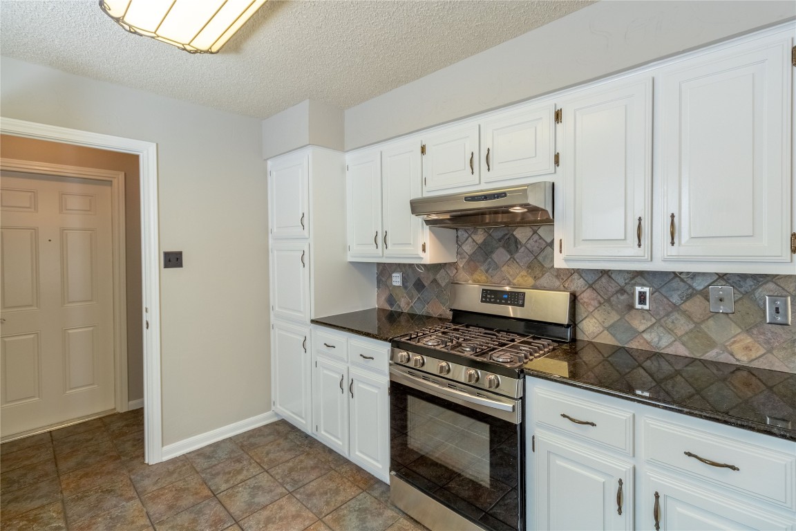 5839 Secrest Drive Austin, TX 78759 - Photo 24 of 34 Kitchen with stainless steel gas range oven, under cabinet range hood, decorative backsplash, white cabinets, and a textured ceiling