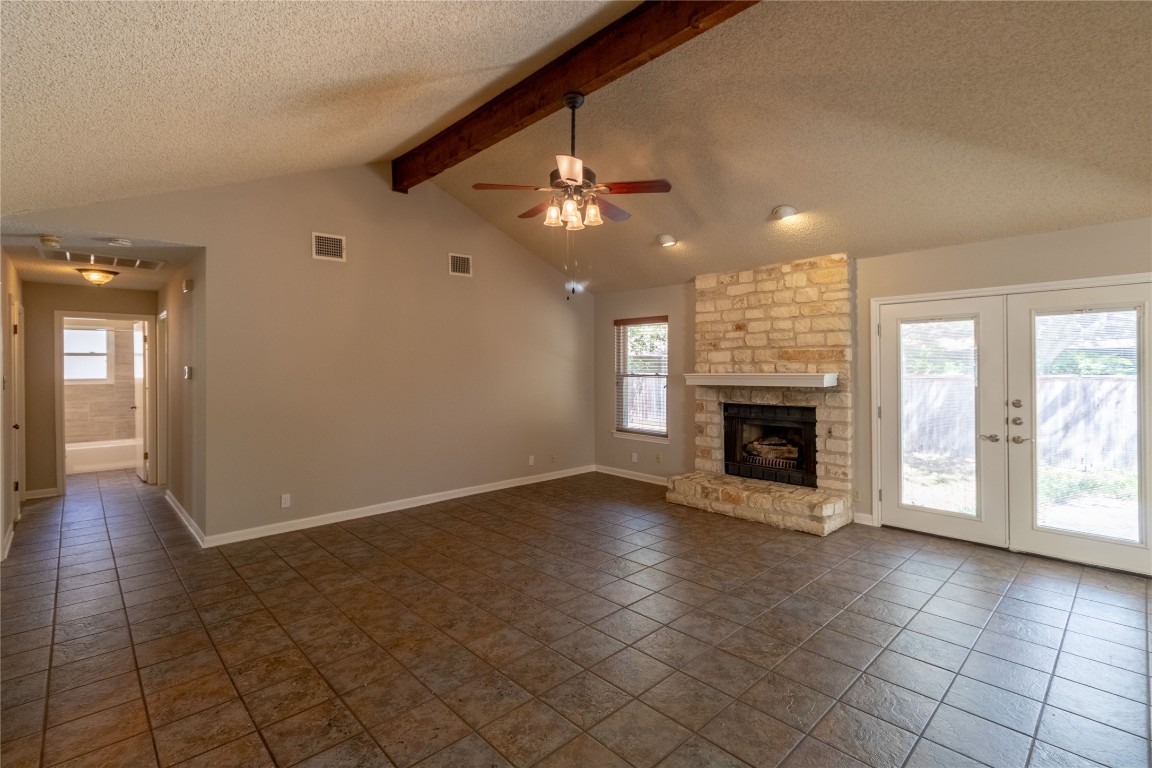 5839 Secrest Drive Austin, TX 78759 - Photo 33 of 34 Unfurnished living room with a textured ceiling, ceiling fan, dark tile patterned flooring, a stone fireplace, and french doors