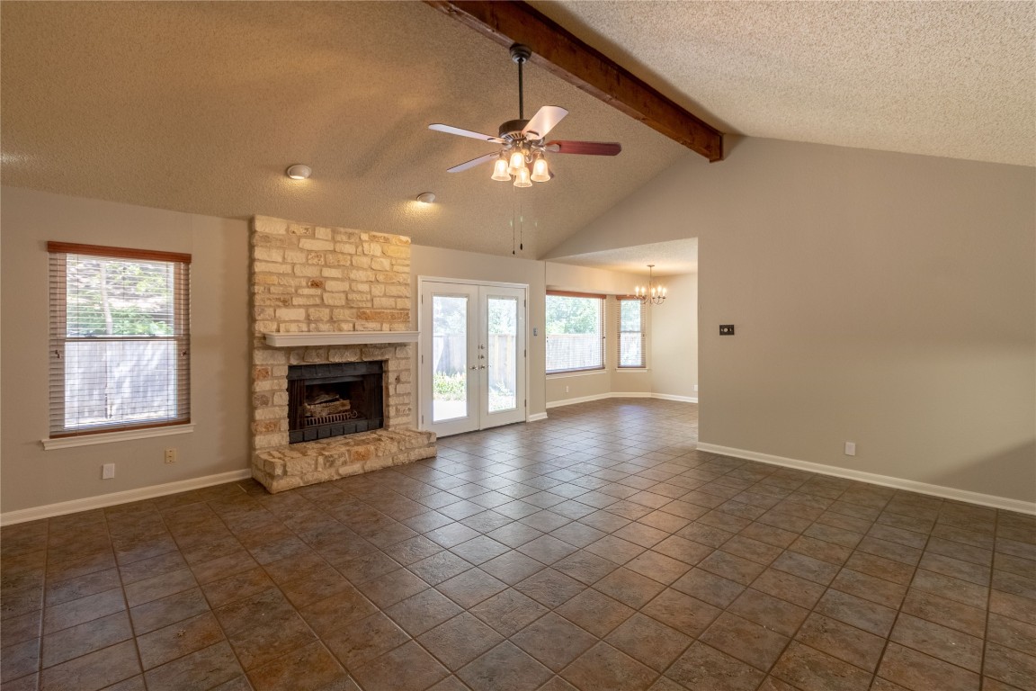 5839 Secrest Drive Austin, TX 78759 - Photo 34 of 34 Unfurnished living room with a textured ceiling, a stone fireplace, a ceiling fan, a chandelier, and dark tile patterned flooring