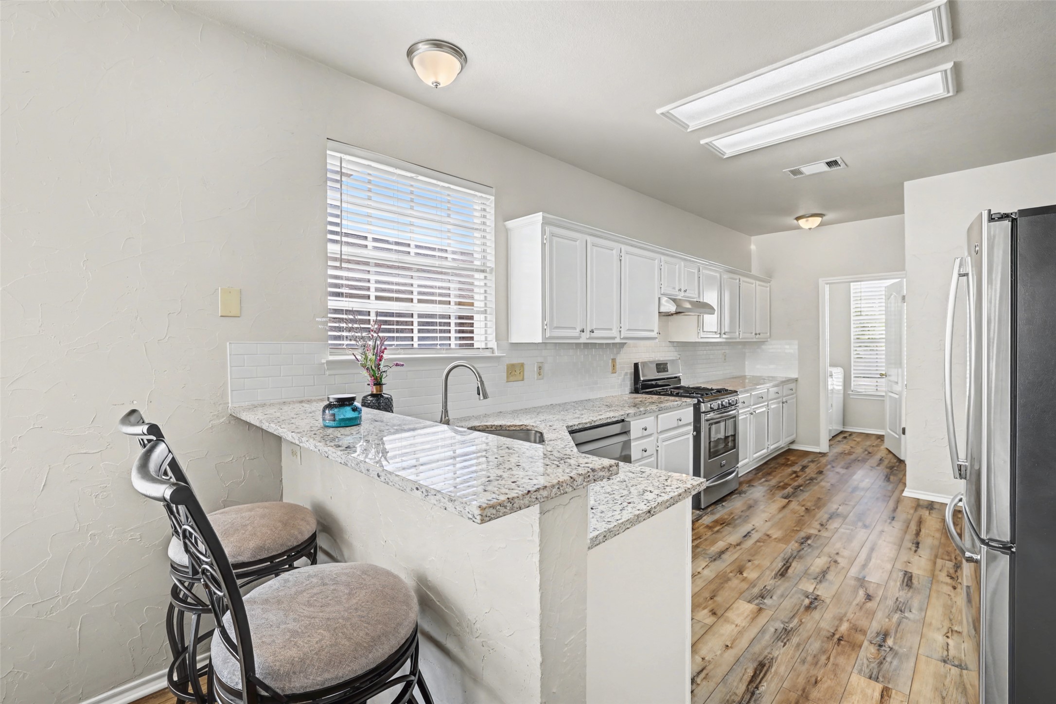 1109 Pebble Brook Road Cedar Park, TX 78613 - Photo 13 of 40 Kitchen featuring a kitchen bar, stainless steel appliances, white cabinetry, tasteful backsplash, and a textured wall