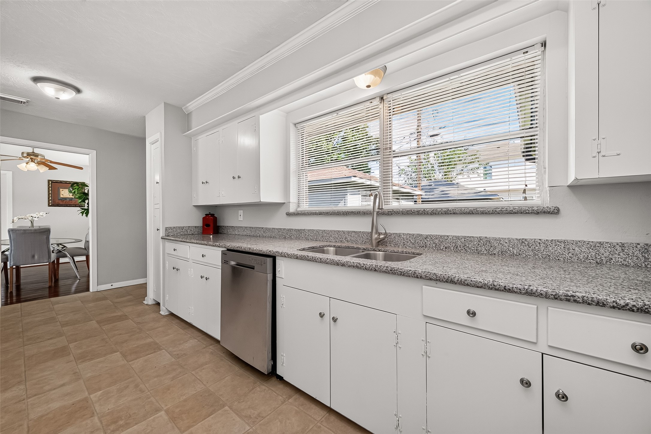 Spacious kitchen with sleek granite countertops, ample cabinetry, and a large window for natural light, flowing into an elegant dining area.