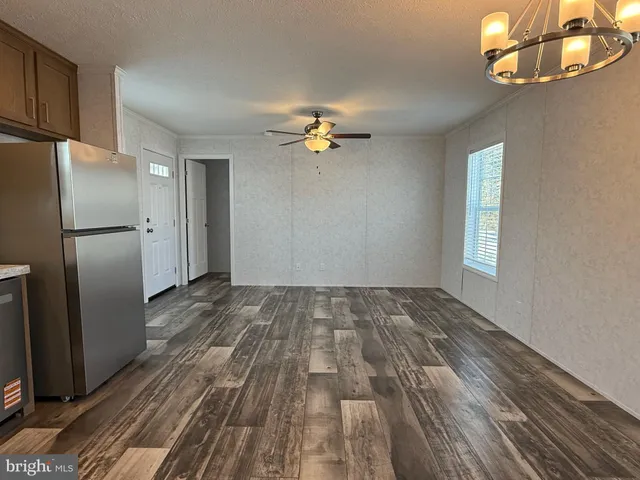 an empty room with wooden floor a ceiling fan a kitchen view and a refrigerator