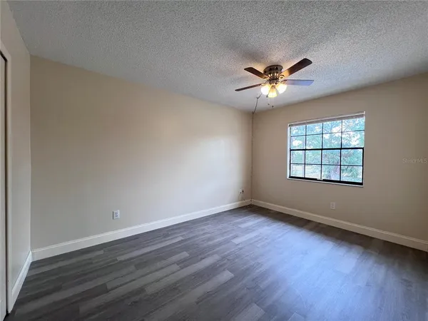 an empty room with wooden floor ceiling fan and windows