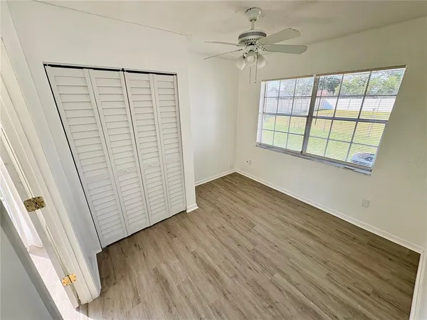 an empty room with wooden floor fan and windows