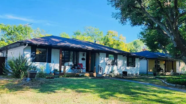 a view of a house with table and chairs under an umbrella with large trees