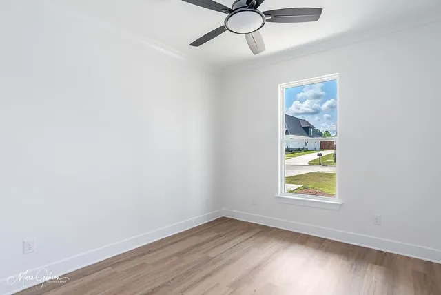 an empty room with wooden floor chandelier fan and windows