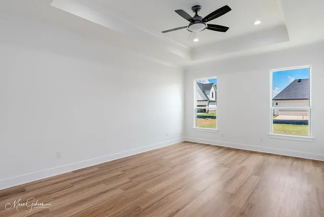 an empty room with wooden floor ceiling fan and windows
