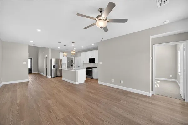 a view of an empty room with wooden floor and a ceiling fan