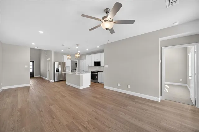 a view of an empty room with wooden floor and a ceiling fan