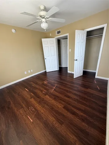 a view of an empty room with wooden floor and a ceiling fan