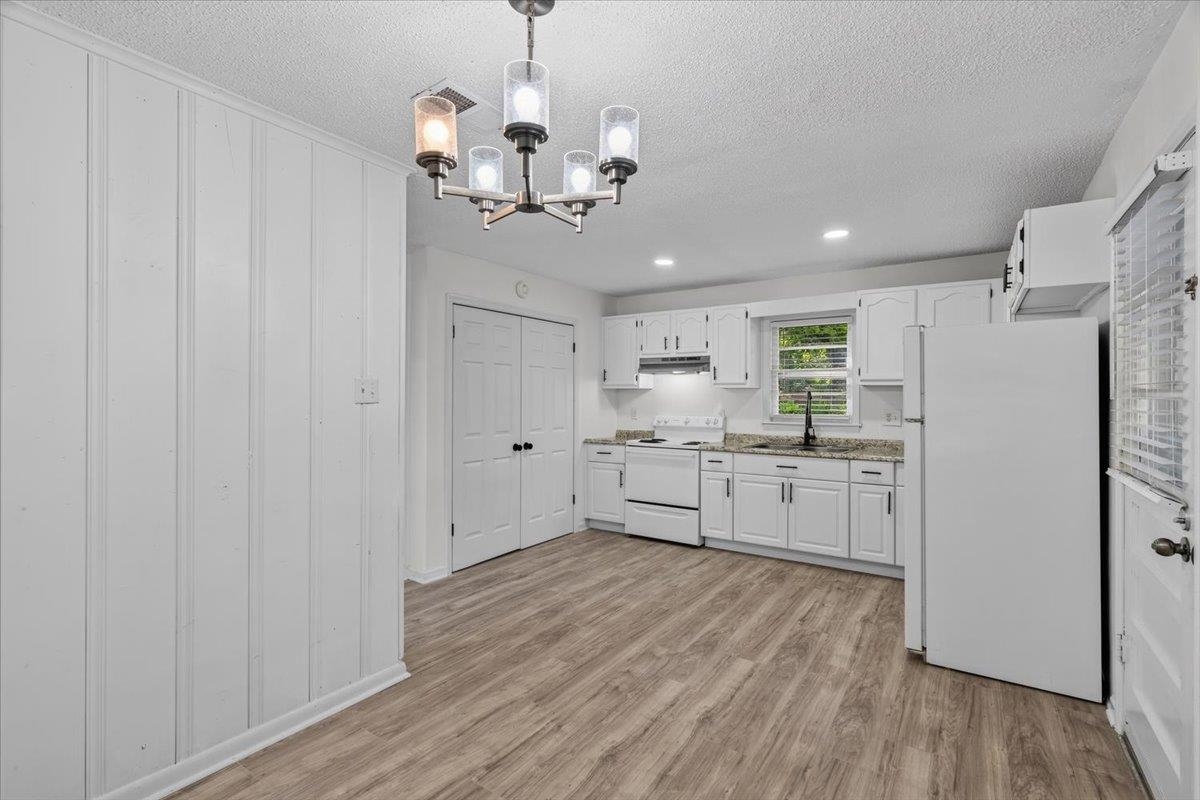 2717 Merle Street Memphis, TN 38118 - Photo 4 of 18 Eat-in kitchen featuring wood-finish flooring, white cabinetry, integrated appliances, and a modern chandelier