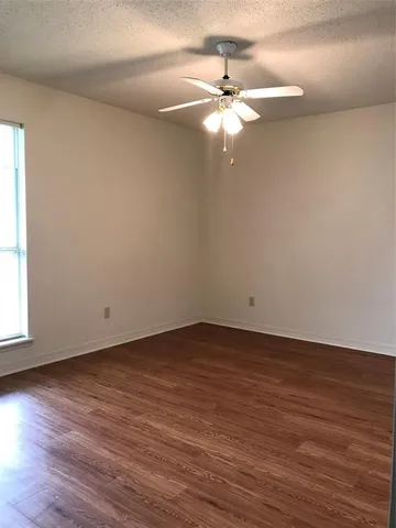 a view of an empty room with wooden floor and fan
