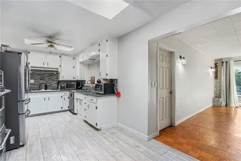 a kitchen with granite countertop a refrigerator a sink dishwasher a stove and white cabinets with wooden floor