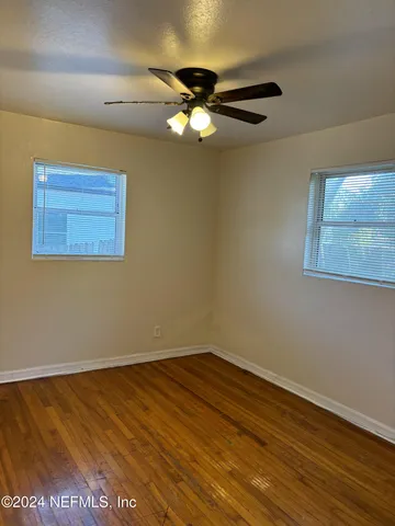 a view of an empty room with wooden floor and a ceiling fan