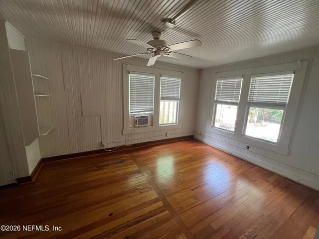 an empty room with wooden floor chandelier fan and windows